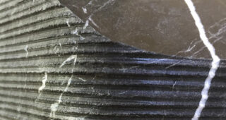 Nahaufnahme einer dunklen, geriffelten Steinoberfläche mit weißen Adern und Linien, die quer durch das Material verlaufen.