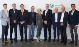 Eine Gruppe von neun Personen in Business-Kleidung steht vor einer Kulisse mit DGNB-Logo und posiert für ein formelles Gruppenfoto.