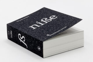 Ein dickes Buch mit schwarz-weiß gesprenkeltem Einband und dem in großen weißen Buchstaben auf der Vorder- und Rückseite aufgedruckten Wort „nife“, das leicht geöffnet auf einer weißen Fläche liegt.