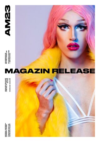 Person mit langen rosa Haaren, auffälligem Make-up und einem weißen Trägertop posiert in einem leuchtend gelben Pelzmantel vor einem blau-violetten Hintergrund mit Farbverlauf. Der Text lautet „MAGAZIN RELEASE“ und „AM23“.
