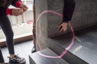 Zwei Personen kleben einen rosa Kreis aus Klebeband an die Ecke einer Steintreppe und richten das Klebeband mit ihren Händen auf den Stufen und der Wand aus.