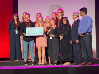 Eine Gruppe von Menschen steht auf der Bühne, einige halten einen großen Scheck über 12.500 US-Dollar mit der Aufschrift „Schneider Go Green Award 2019“ in den Händen.