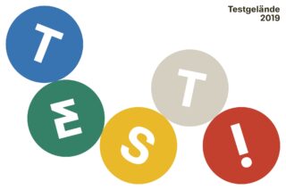 Fünf farbige Kreise mit großen weißen Buchstaben ergeben in verspielter Anordnung „TEST!“, in der oberen rechten Ecke steht „Testgelände 2019“.