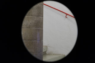 Eine Rundansicht, die einen Teil einer Steinsäule, weiße Treppen, eine weiße Wand und ein rotes Geländer zeigt.