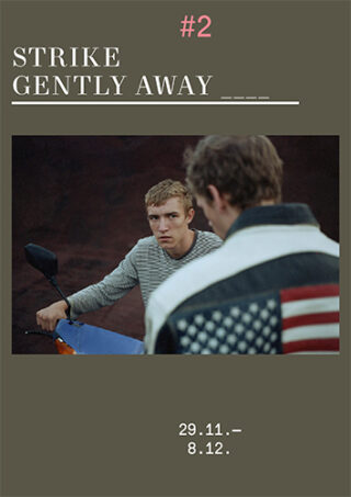 Zwei junge Männer stehen sich gegenüber; einer sitzt auf einem Motorrad, der andere trägt eine Jacke mit einem Aufnäher der US-Flagge. Oben und unten steht ein Text, der für die Veranstaltung „Strike Gently Away #2“ vom 29.11. bis 8.12. wirbt.