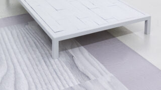 Eine weiße, rechteckige Plattform mit einem geometrischen Oberflächenmuster steht auf einem Boden mit verschiedenen Texturen und Schattierungen von Grau und Hellviolett.