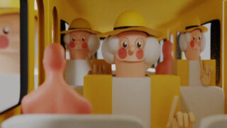 Tonfiguren mit weißen Haaren und gelben Hüten sitzen in einem gelben Bus und blicken nach vorne. Die Szene ist in einem verspielten, cartoonhaften Stil gehalten.
