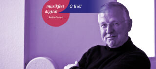 Ein älterer Mann mit Brille und dunklem Pullover sitzt im Haus. Darüber hängt ein Banner mit der Aufschrift „musikfest digital & live! Audio-Podcast“. Das Bild ist violett gefärbt.
