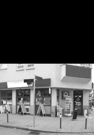 Eine Straßenansicht eines Ladens mit leeren Schildern, mehreren Sandwich-Tafeln auf dem Bürgersteig und einem Mast mit Straßenschildern davor.