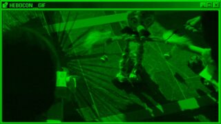 Ein grün getöntes Bild zeigt einen selbstgebauten Roboter mit langer Nase und gefiederten Armen auf einem gefliesten Boden, von oben betrachtet. Links ist eine Teilansicht eines weiteren Objekts zu sehen.