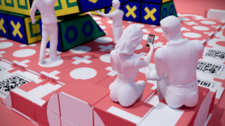 Zwei weiße Statuen sitzen auf rot-weißen Blöcken. Eine davon hält ein Telefon mit einem QR-Code. Weitere Statuen stehen in der Nähe, umgeben von großen geometrischen Blöcken und QR-Code-Mustern auf dem Boden.