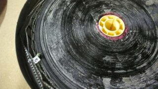 Eine Nahaufnahme einer großen schwarzen Rolle mit gelber Mitte und einem weißen Etikett mit der Aufschrift „5“ am Rand, die auf einer hellbraunen Oberfläche liegt.