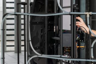 Eine Person passt die Verkabelung und die elektronischen Komponenten eines großen Geräts oder einer Maschine mit Metallrahmen an, wobei Kabel und Paneele in einer modernen Industrieumgebung sichtbar sind.