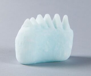 Ein hellblaues, strukturiertes Objekt mit fünf kegelförmigen Spitzen steht auf einer grauen Oberfläche vor einem neutralen Hintergrund.