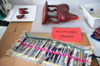 Auf einem Tisch neben einer roten Skulptur und einem roten Schild mit der Aufschrift „ACHTUNG Objekt!“ liegt ein Satz Konservierungswerkzeuge bereit, das vor einem empfindlichen Objekt in der Nähe warnt.