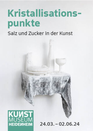 Ein weißer Tisch mit Flaschen, einem Teller und einem mit Salz oder Zucker bedeckten Glas wirbt für eine Kunstausstellung mit dem Titel „Kristallisationspunkte“ im Kunstmuseum Heidenheim.