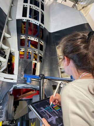 Eine Person verwendet einen Stift und ein Tablet, um eine detaillierte Schnittansicht der inneren Struktur eines Flugzeugs zu analysieren oder zu zeichnen.