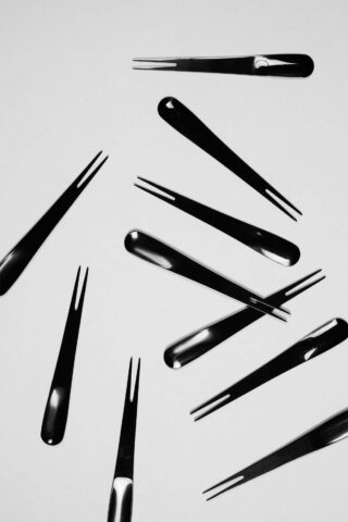 Mehrere schwarze Cocktailgabeln mit zwei Zinken liegen verstreut auf einer schlichten, hellen Oberfläche.