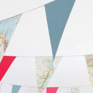 Bunte dreieckige Wimpel, einige mit Karten bedruckt, hängen an Schnüren vor einem weißen Hintergrund.