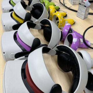 Auf einem hellen Holztisch sind eine Reihe von Virtual-Reality-Headsets mit bunten Kopfbändern und Controllern angeordnet.