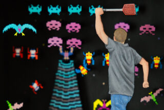 Eine Person mit einer Fliegenklatsche blickt auf einen Bildschirm, auf dem pixelige Space Invaders aus einem Retro-Arcade-Videospiel zu sehen sind.