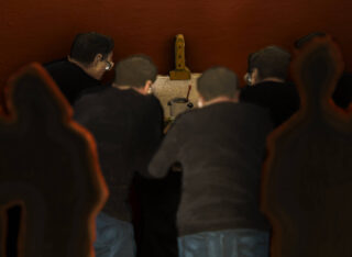 Fünf Personen stehen dicht beieinander vor einem kleinen Tisch oder einer Vitrine mit Werkzeugen und einem Gegenstand vor einem rotbraunen Hintergrund. An den Rändern sind zwei schemenhafte Silhouetten zu erkennen.