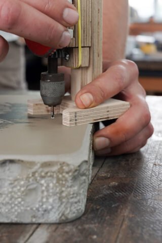 Eine Person verwendet eine kleine Bohrmaschine, um die Oberfläche einer Steinplatte auf einer hölzernen Werkbank zu gravieren oder zu schnitzen.