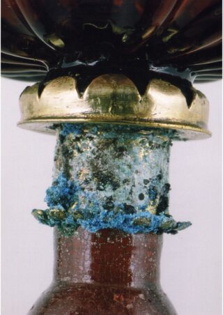 Nahaufnahme eines Metallrandes einer braunen Flasche mit sichtbarer blauer Korrosion und Oxidation am Hals direkt unter dem Metall.