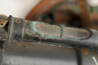 Nahaufnahme einer korrodierten und verwitterten Metalloberfläche, möglicherweise Teil einer Maschine oder eines Werkzeugs, mit grünlich oxidierten Flecken.