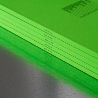 Eine Nahaufnahme von sechs gestapelten hellgrünen Ordnern oder Mappen auf einer metallischen Oberfläche, die am Rand jeweils mit ähnlichen alphanumerischen Codes beschriftet sind.