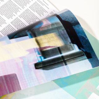 Eine Nahaufnahme einer farbig bedruckten Zeitschriftenseite, die umgeblättert wird und Text und ein Halbtonbild mit überlappenden Farben und Punktmustern zum Vorschein bringt.