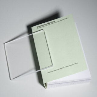 Ein Stapel hellgrüner Papiere mit der Aufschrift „Gemischte Wombos“, auf dem teilweise eine durchsichtige rechteckige Acrylplatte liegt.