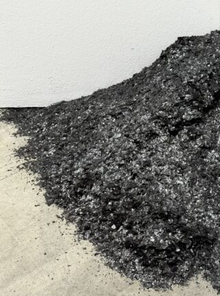 Ein Haufen schwarzer und silberner Metalltrümmer ist vor einer weißen Wand aufgestapelt und über einen Betonboden verteilt.