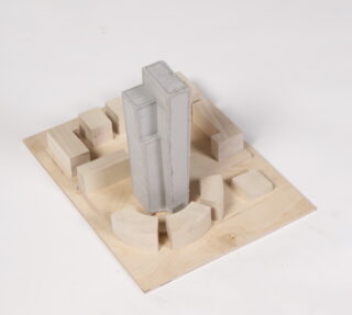 Ein Tischarchitekturmodell mit einer zentralen, hohen, rechteckigen Betonstruktur, die von kleineren Gebäuden aus Holzblöcken auf einer quadratischen Basis umgeben ist.