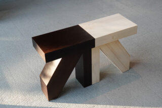 Eine Holzbank mit geometrischem Design und kontrastierenden dunklen und hellen Holzabschnitten, platziert auf einem strukturierten hellen Teppich.