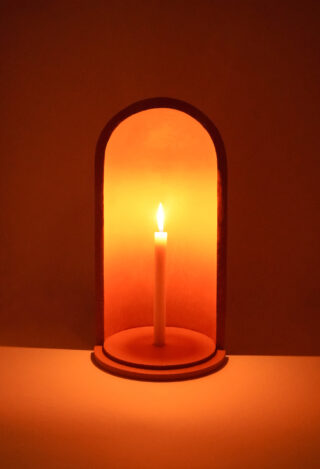 In einer kleinen, gewölbten Nische brennt eine einzelne weiße Kerze und wirft einen warmen orangefarbenen Schein auf die umgebende Wand.