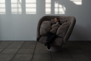 Eine Person sitzt bequem in einem großen, gepolsterten Stuhl neben einer weißen Wand mit Fensterschatten darauf.