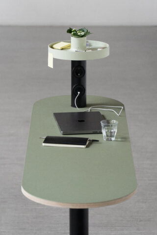 Ein minimalistischer Schreibtisch mit einem geschlossenen Laptop, einem Notizbuch, einem Stift, einem Glas Wasser und einem erhöhten Regal mit einer kleinen Topfpflanze, Haftnotizen und einem Bleistift.