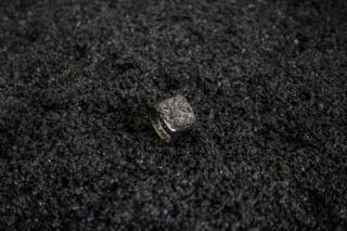 Ein strukturierter Metallring liegt auf einer rauen, schwarzen, körnigen Oberfläche.