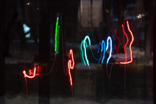 Verschwommene Neonlichter in Rot, Grün und Blau bilden abstrakte, wellenförmige Linien vor einem dunklen Hintergrund.