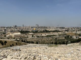 Blick auf Jerusalem mit dem Felsendom in der Mitte, historischen Mauern und einem großen Friedhof im Vordergrund unter klarem Himmel.