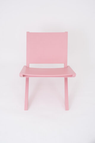 Ein einfacher rosa Holzstuhl mit flacher Sitzfläche und Rückenlehne, fotografiert vor einem schlichten weißen Hintergrund.