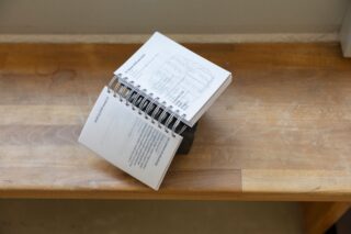 Ein spiralgebundenes Büchlein ist auf einer hölzernen Oberfläche aufgeschlagen und zeigt Bild- und Textseiten.