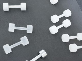 Mehrere weiße und eine metallische Hantel sind auf einer dunkelgrauen Fläche angeordnet.