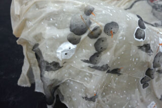 Transparenter Stoff mit einem aufgedruckten Muster aus Schneemännern, Schnee und verstreuten schwarzen Formen, der über eine Fläche drapiert ist.