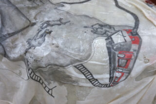 Nahaufnahme einer illustrierten Karte, die einen roten Zug auf Schienen zeigt, mit skizzenhaften Umrissen von Land und kurvigen Wegen in Schwarz- und Grautönen.