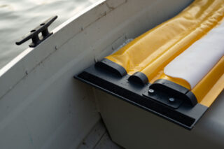 Nahaufnahme der Ecke eines weißen Bootes mit einem gelben und weißen aufblasbaren Kissen auf dem Sitz in der Nähe einer Metallklampe. Außerhalb des Bootes ist Wasser zu sehen.