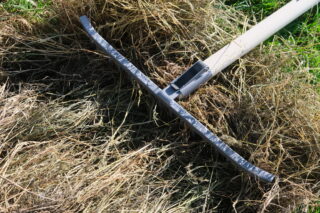 Ein Metallrechen liegt auf einem Haufen trockenen Grases und Heus auf dem Boden.