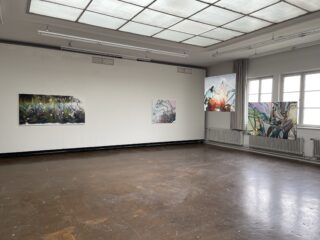 Ein karger Galerieraum mit fünf abstrakten Gemälden an weißen Wänden, großen Fenstern und einem braunen Boden. Natürliches Licht erfüllt den Raum.