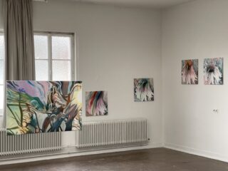 Galerieraum mit fünf abstrakten Gemälden an weißen Wänden, von denen eines vor einem Fenster und einem Heizkörper hängt, mit Holzfußboden und teilweise geöffnetem beigen Vorhang.